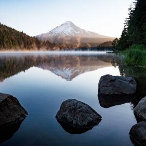 calm body of water with rocks near trees and mountain