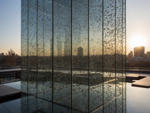 AP Glass A tall glass building with visible etched patterns and birds flying nearby.