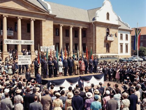Diverse officials and a festive crowd at a government ceremony outside a Cape Town building.